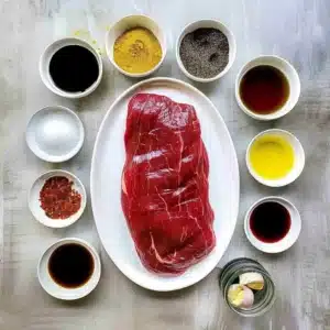 Raw flank steak with marinade ingredients in small bowls